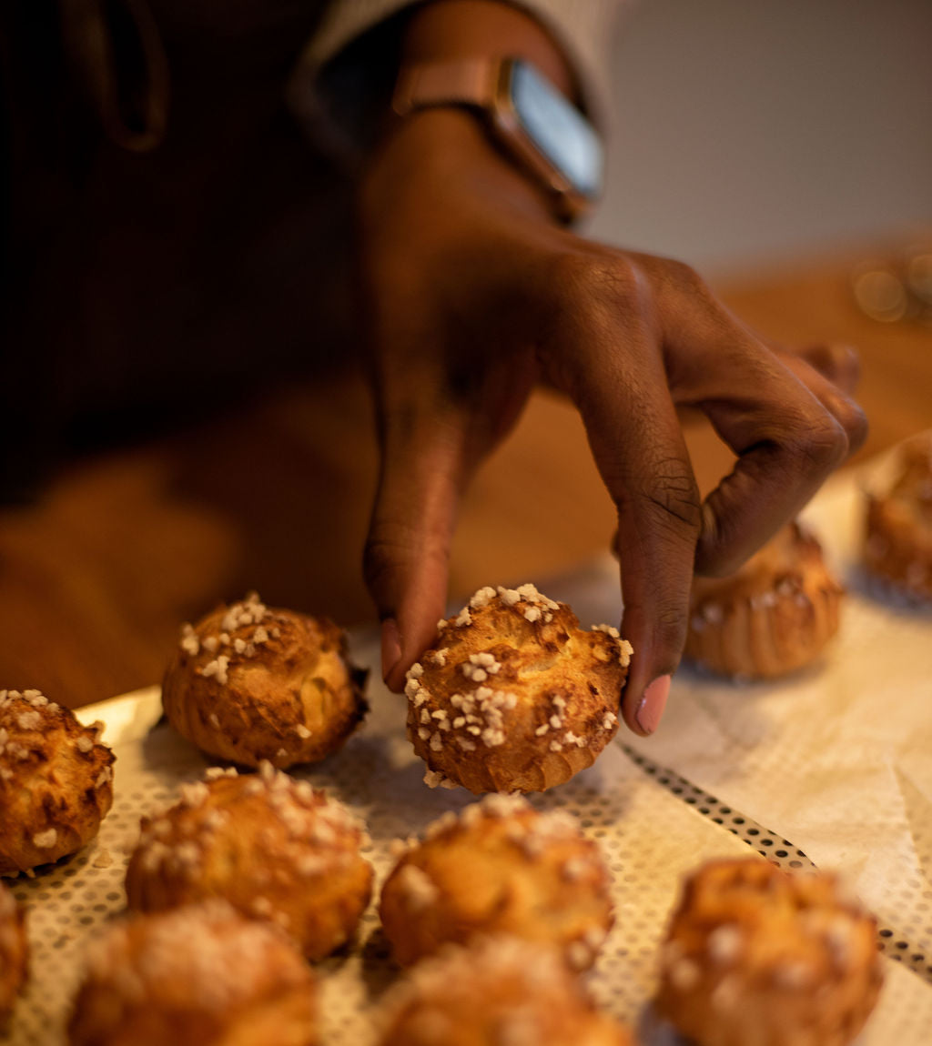 Hand picking up a golden choux bun topped with pearl sugar from a baking mat during an eclair and choux pastry class at Maison Fleuret Paris