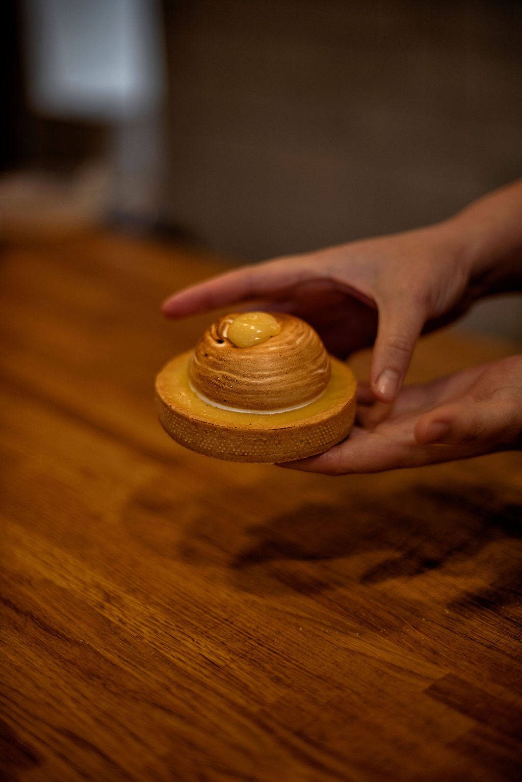 Hand holding a finished lemon meringue tart with an elegant torched swirled meringue dome and a lemon curd drop on top, made during a pastry class at Maison Fleuret Paris