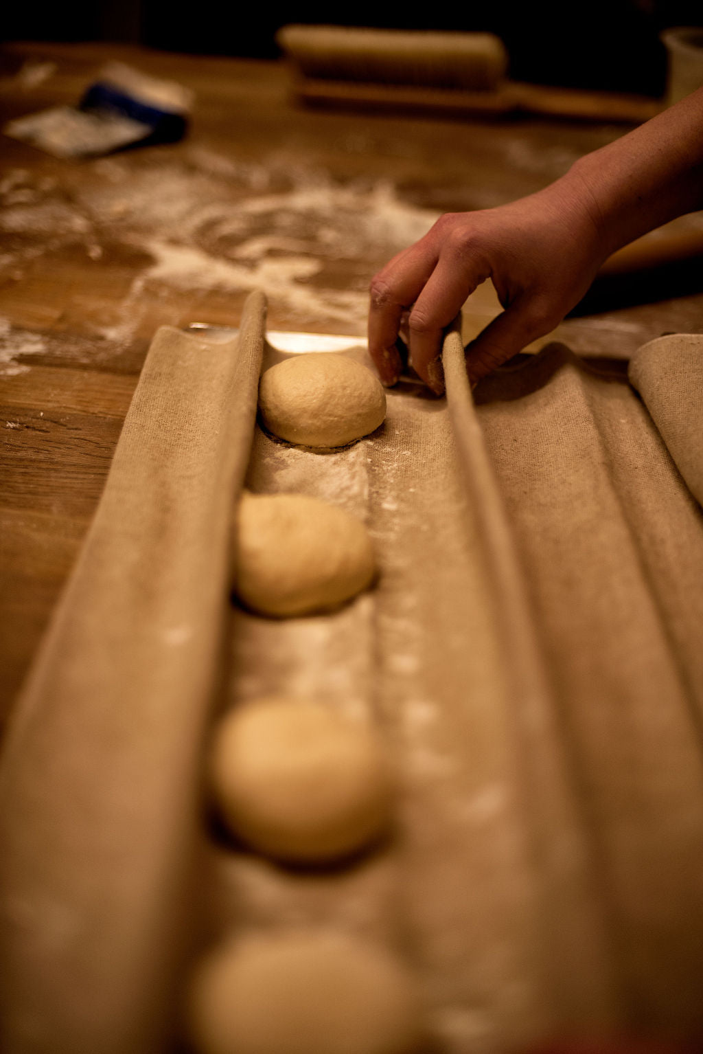 Hand placing rounded bread dough balls into a linen couche for proofing on a flour-dusted wooden table during a baguette baking class at Maison Fleuret Paris