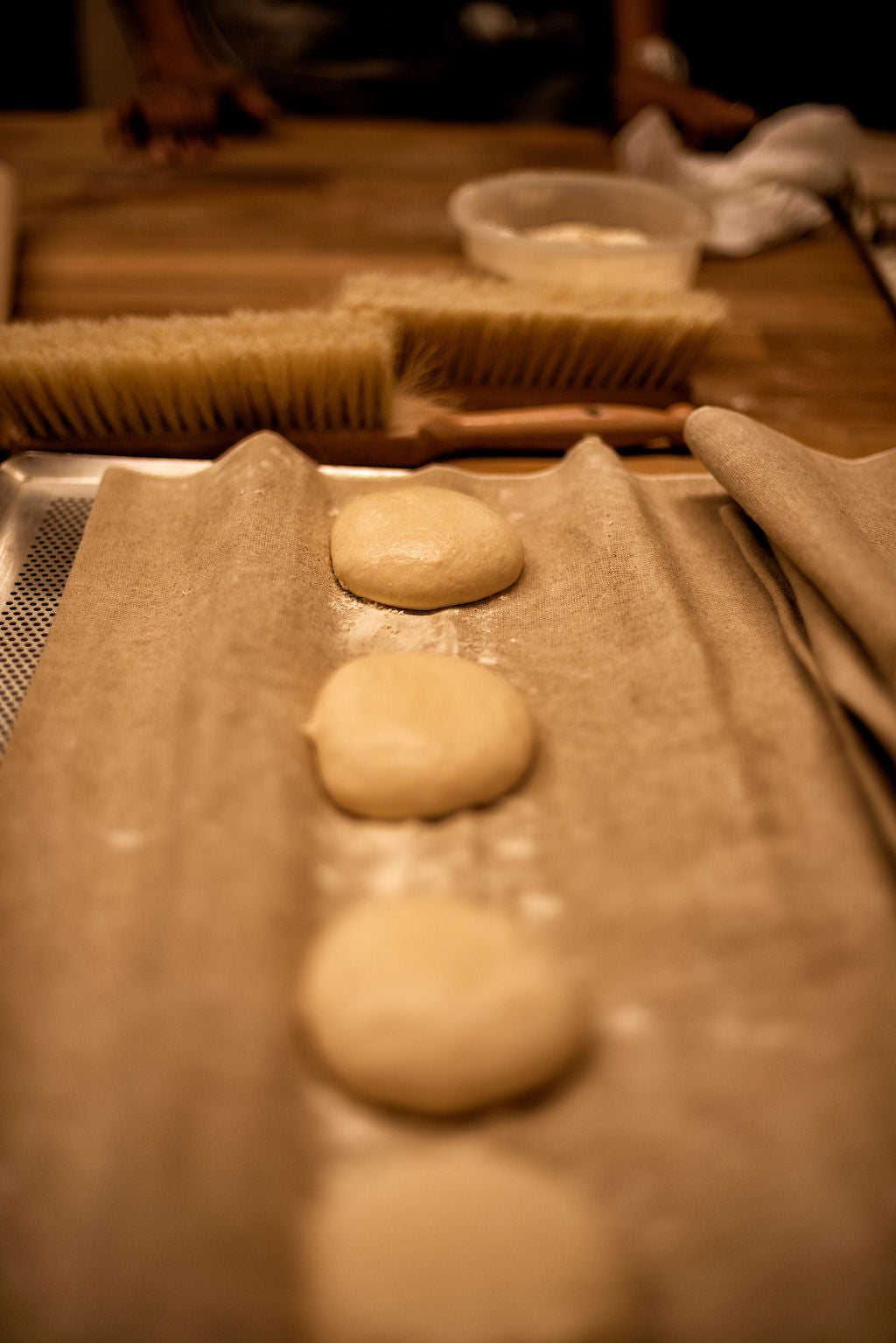 Bread dough balls proofing in a linen couche on a perforated baking tray with a flour brush and sourdough starter in the background during a baguette class at Maison Fleuret Paris