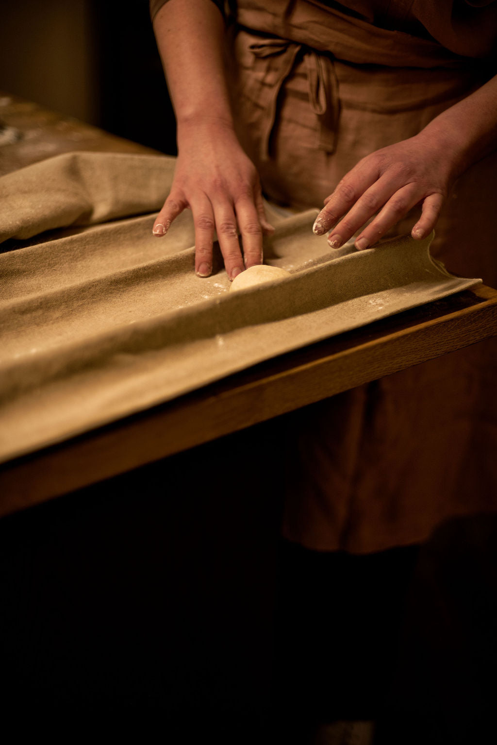 Participant in apron rolling bread dough by hand on a linen couche during a hands-on baguette shaping class at Maison Fleuret Paris near Notre-Dame
