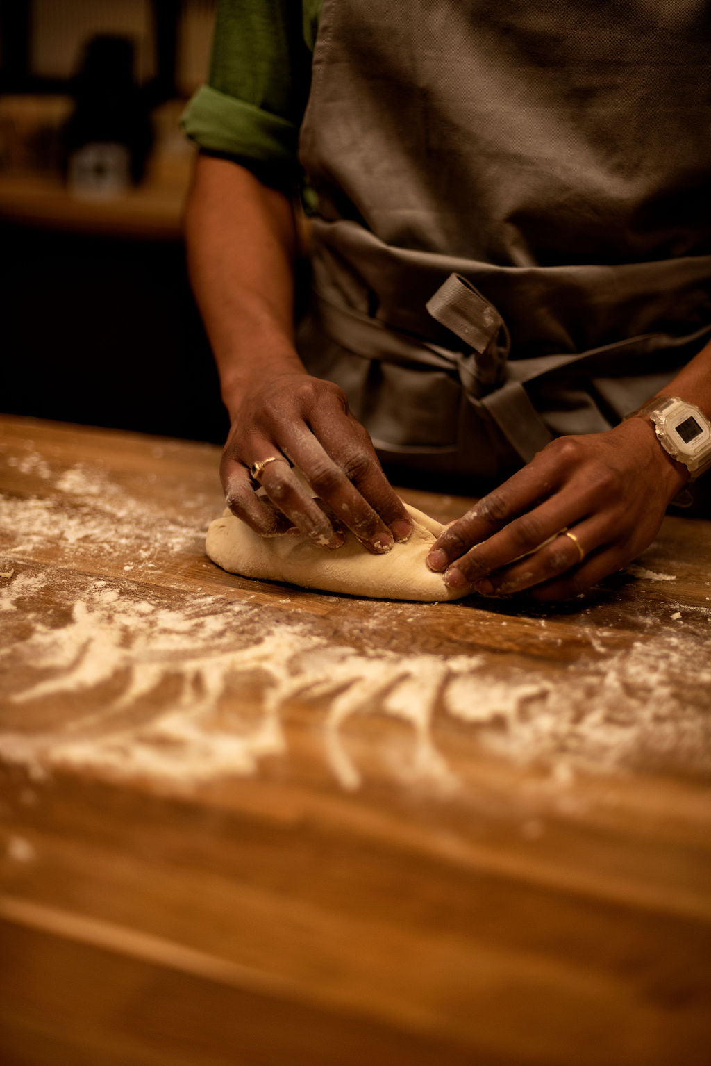 Participant kneading bread dough by hand on a flour-dusted wooden worktop wearing an apron during a hands-on baguette baking class at Maison Fleuret Paris