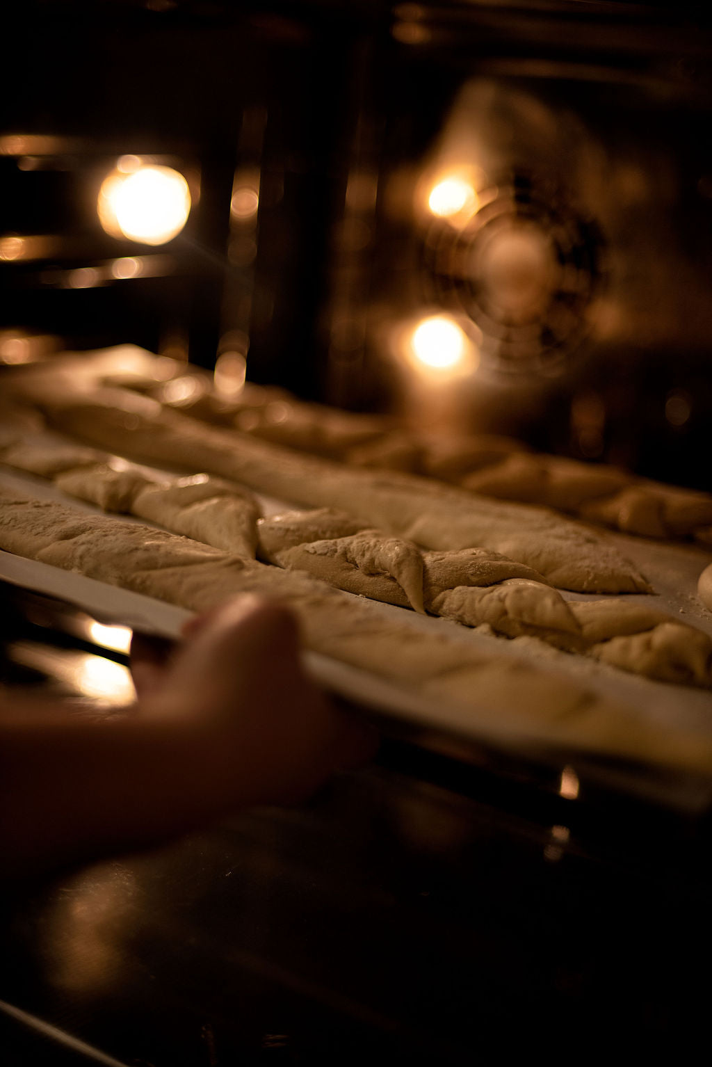 Scored baguettes being slid into a professional convection oven with warm light during a French bread baking class at Maison Fleuret Paris near Notre-Dame