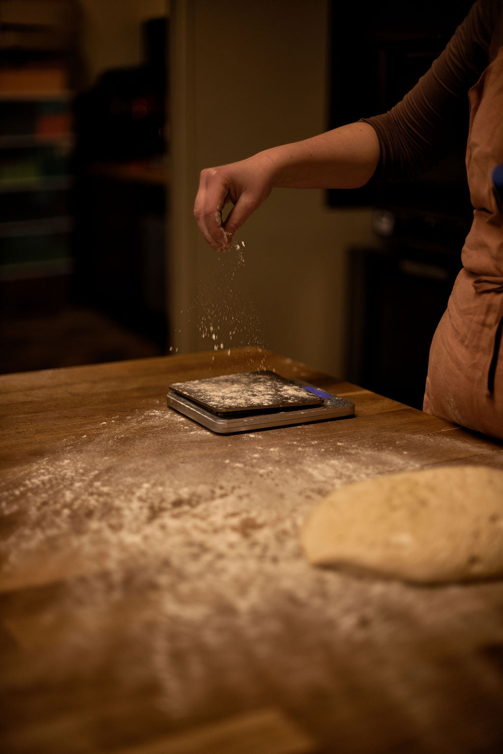 Baker in apron sprinkling flour over a digital scale on a flour-dusted wooden worktop with bread dough during a baguette baking class at Maison Fleuret Paris