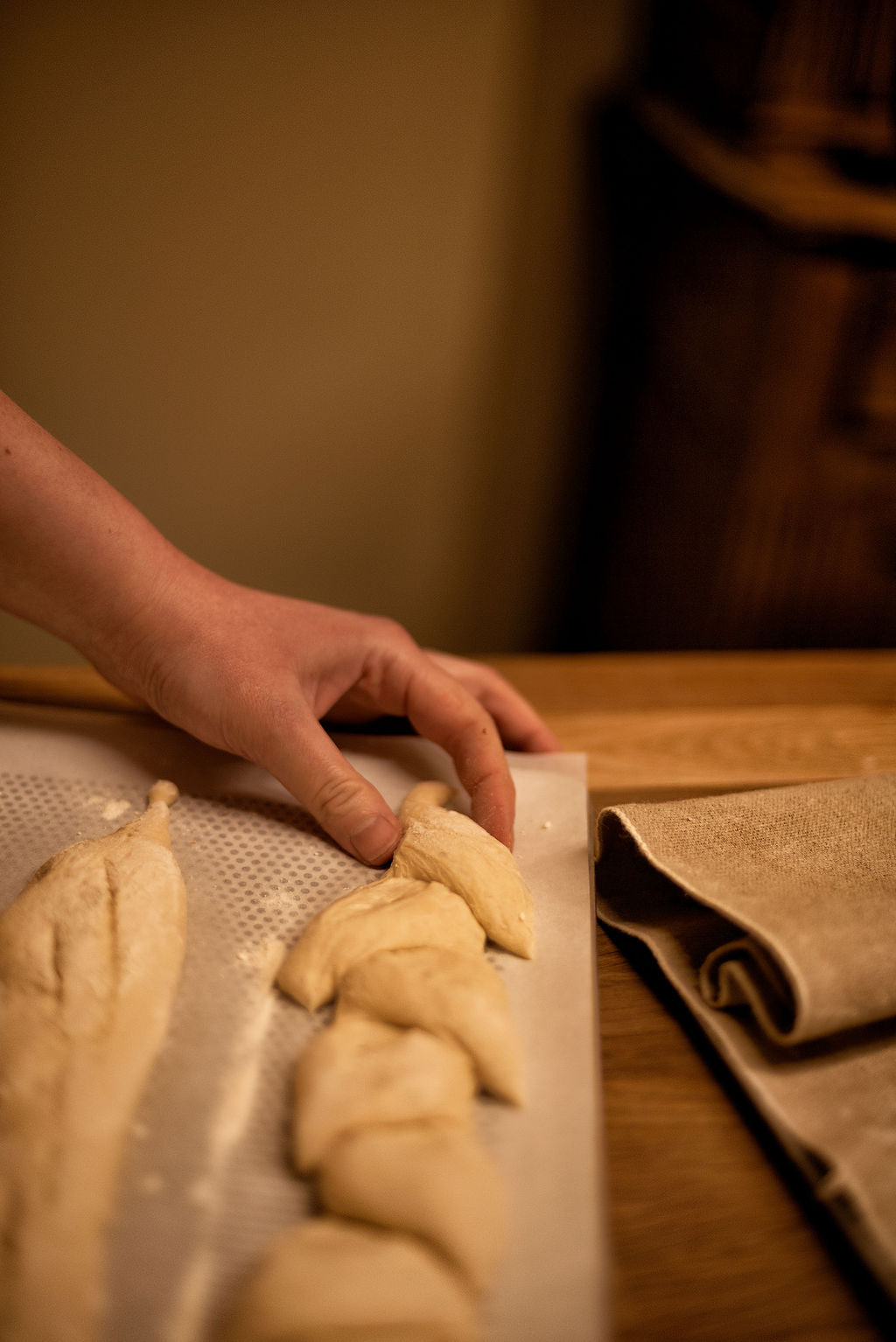 Hand placing twisted bread dough shapes onto a perforated baking mat with a folded linen couche beside during a baguette baking class at Maison Fleuret Paris