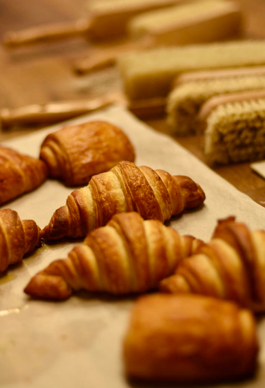 Golden flaky croissants and pains au chocolat freshly baked on parchment paper alongside sliced cakes during a hands-on croissant baking class at Maison Fleuret Paris