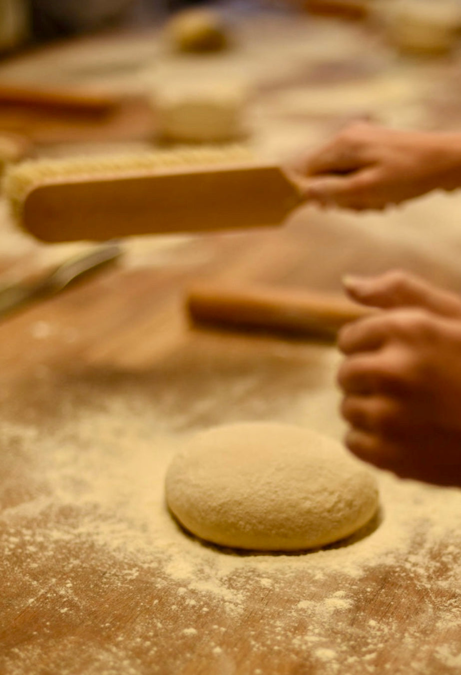 Participant about to roll out a round croissant dough ball with a wooden rolling pin on a heavily flour-dusted worktop during a hands-on croissant baking class at Maison Fleuret Paris