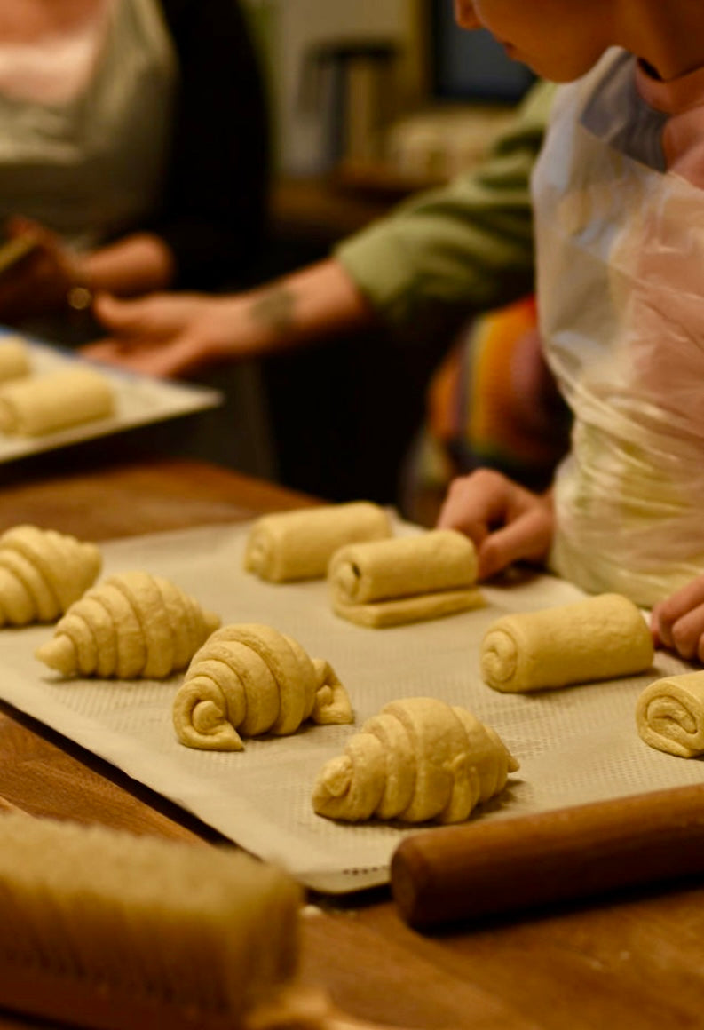 Shaped raw croissants, pains au chocolat, and pains aux raisins arranged on a silicone baking mat with participants placing the last pieces before baking during a croissant class at Maison Fleuret Paris