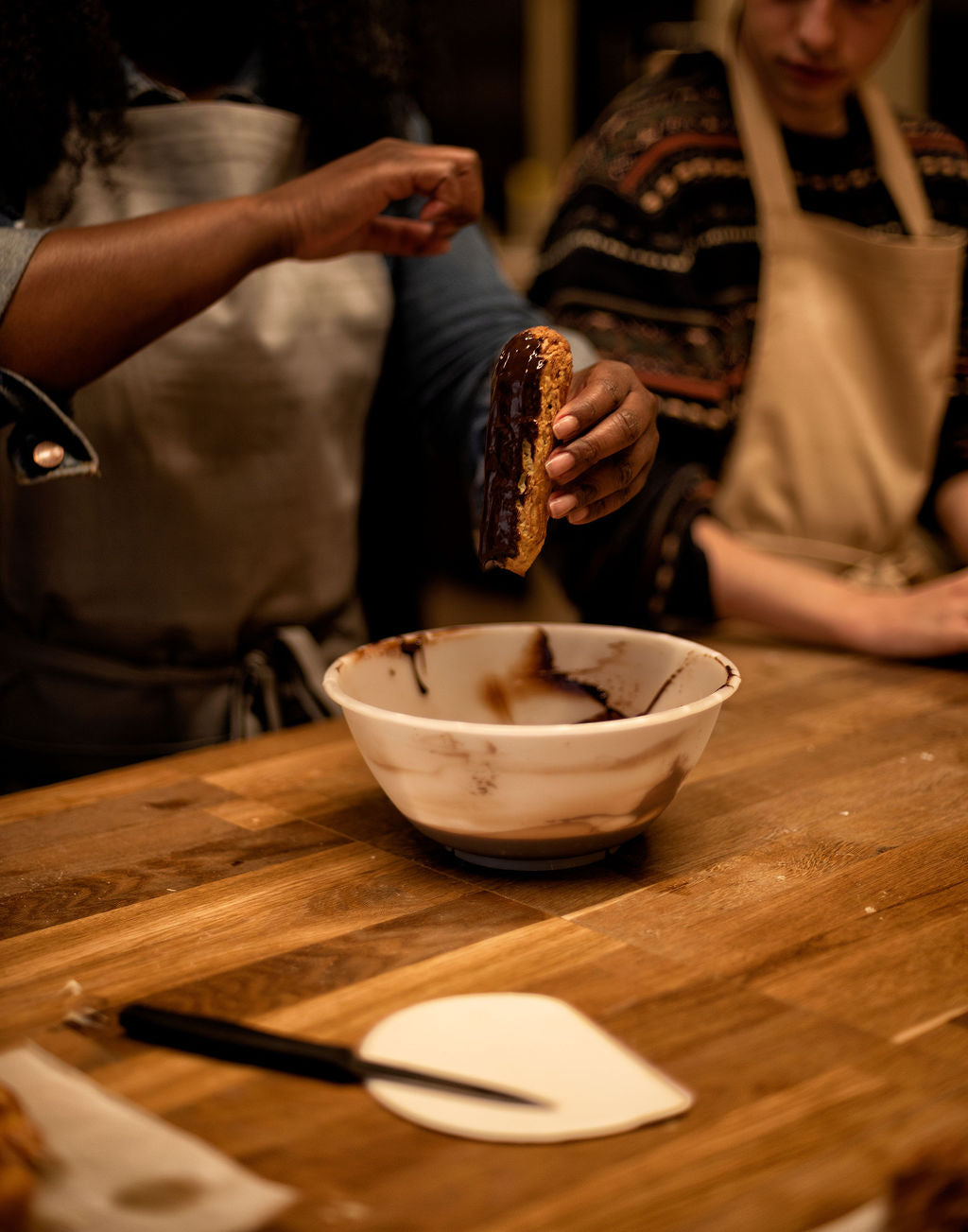 Hands decorating eclairs with chocolate glaze during a hands-on French pastry class in Paris