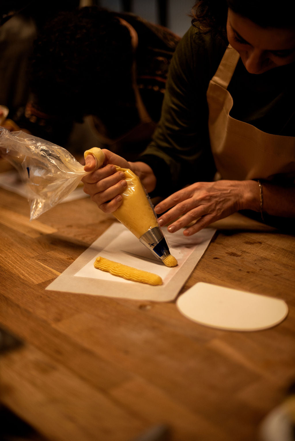 Participant piping eclair-shaped choux dough with a pastry bag and metal tip onto parchment paper during a hands-on eclair class at Maison Fleuret Paris