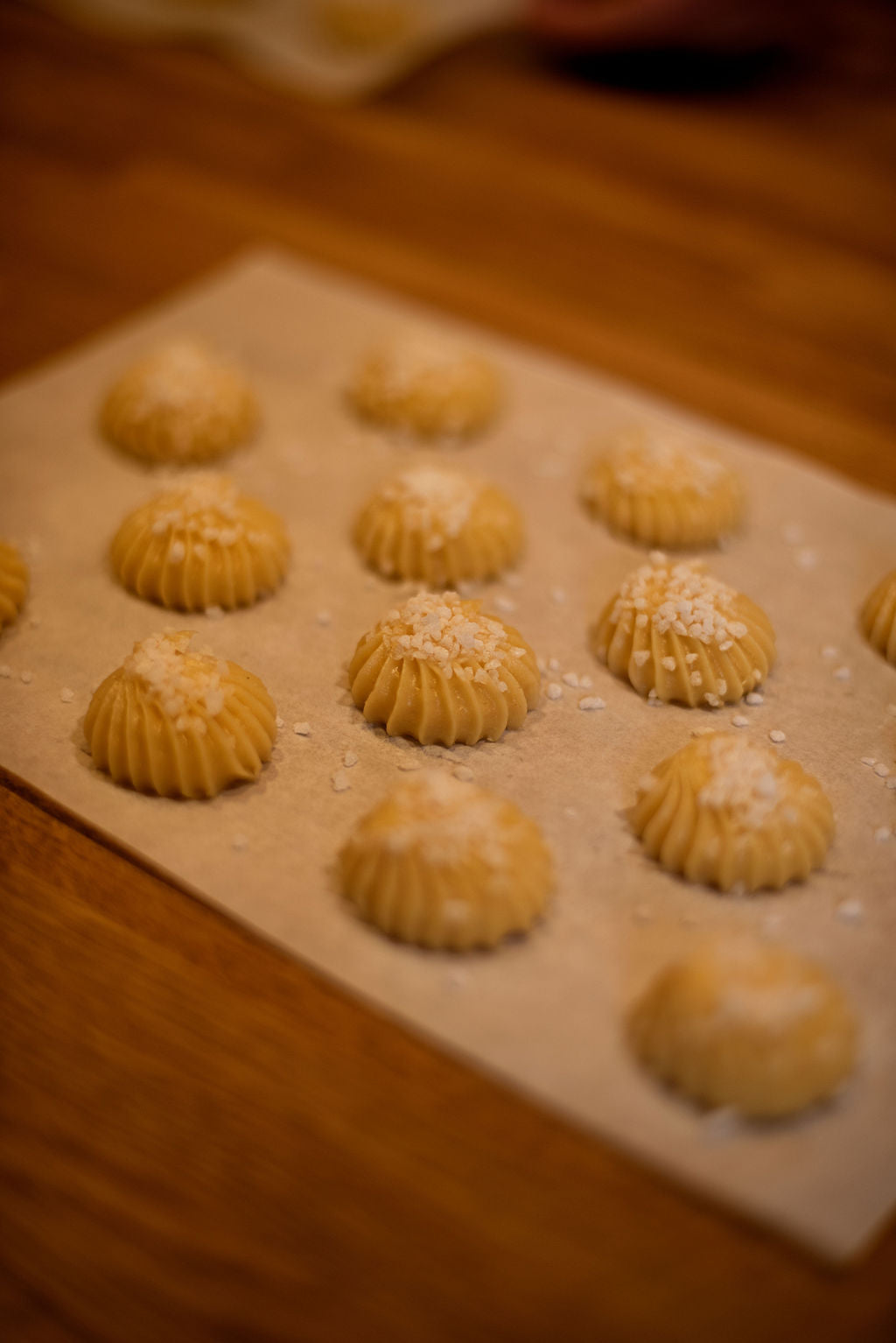 Perfectly piped choux buns with ridged pattern topped with pearl sugar on parchment paper before baking during an eclair and choux class at Maison Fleuret Paris
