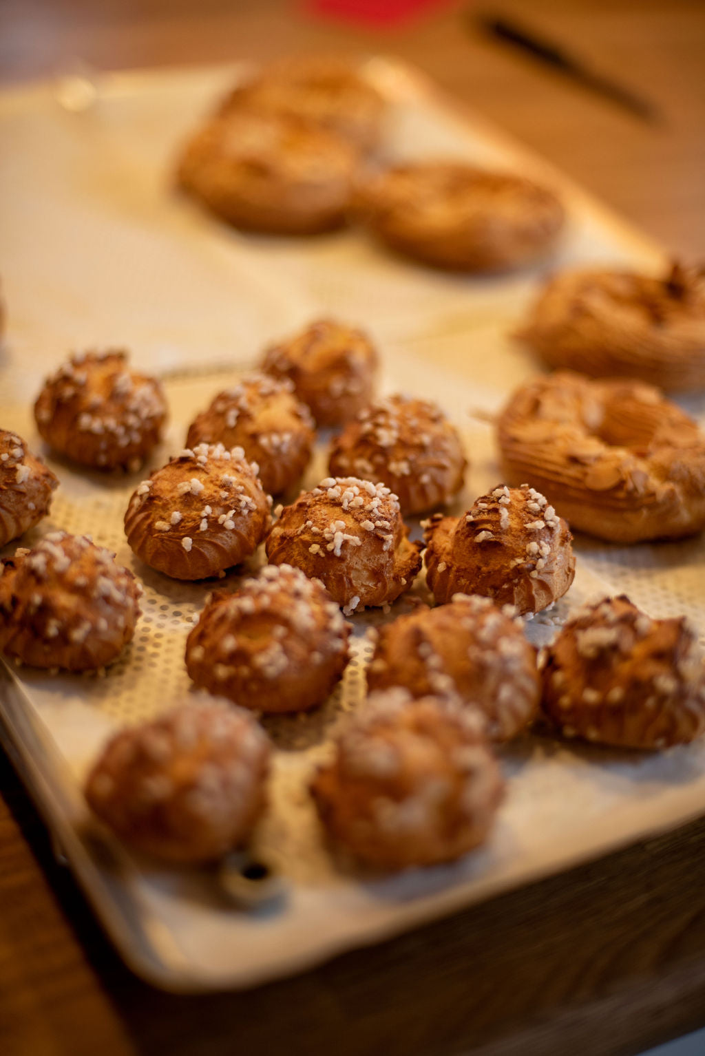 Tray of freshly baked golden choux buns with pearl sugar and eclairs cooling on a perforated baking mat during a Paris pastry class at Maison Fleuret