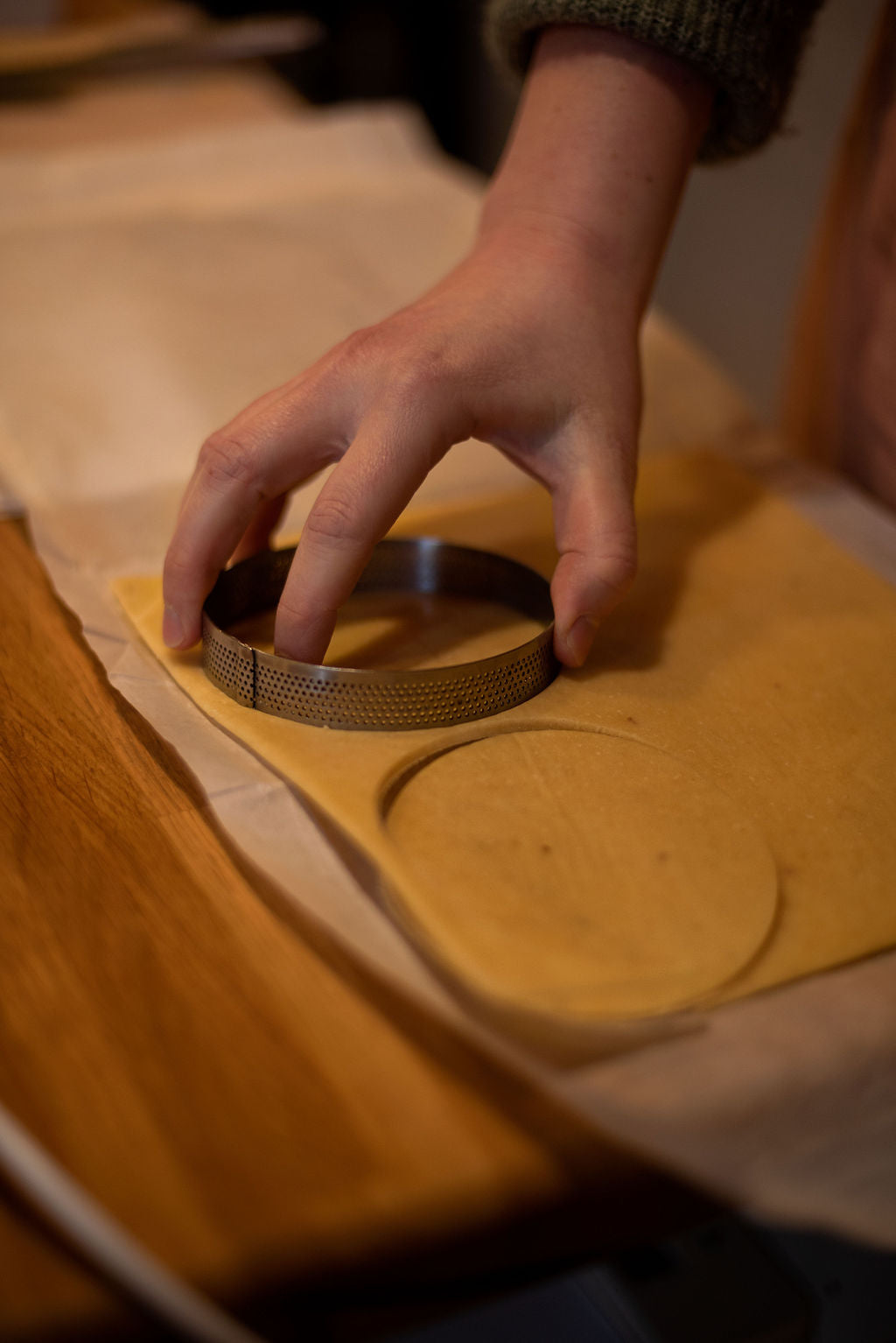 Hand pressing a perforated metal tart ring into rolled-out shortcrust pastry dough to cut tart bases during a lemon meringue tart class at Maison Fleuret Paris