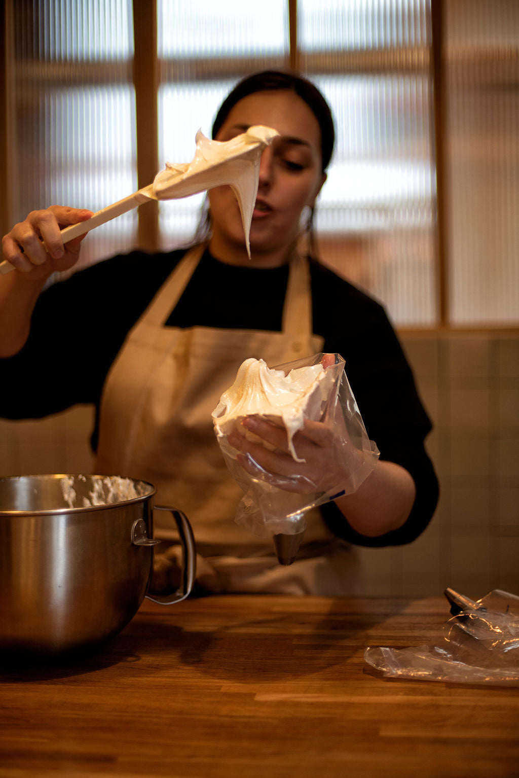 Participant in apron transferring glossy Italian meringue from a mixing bowl into a piping bag with a wooden spatula during a lemon meringue tart class at Maison Fleuret Paris