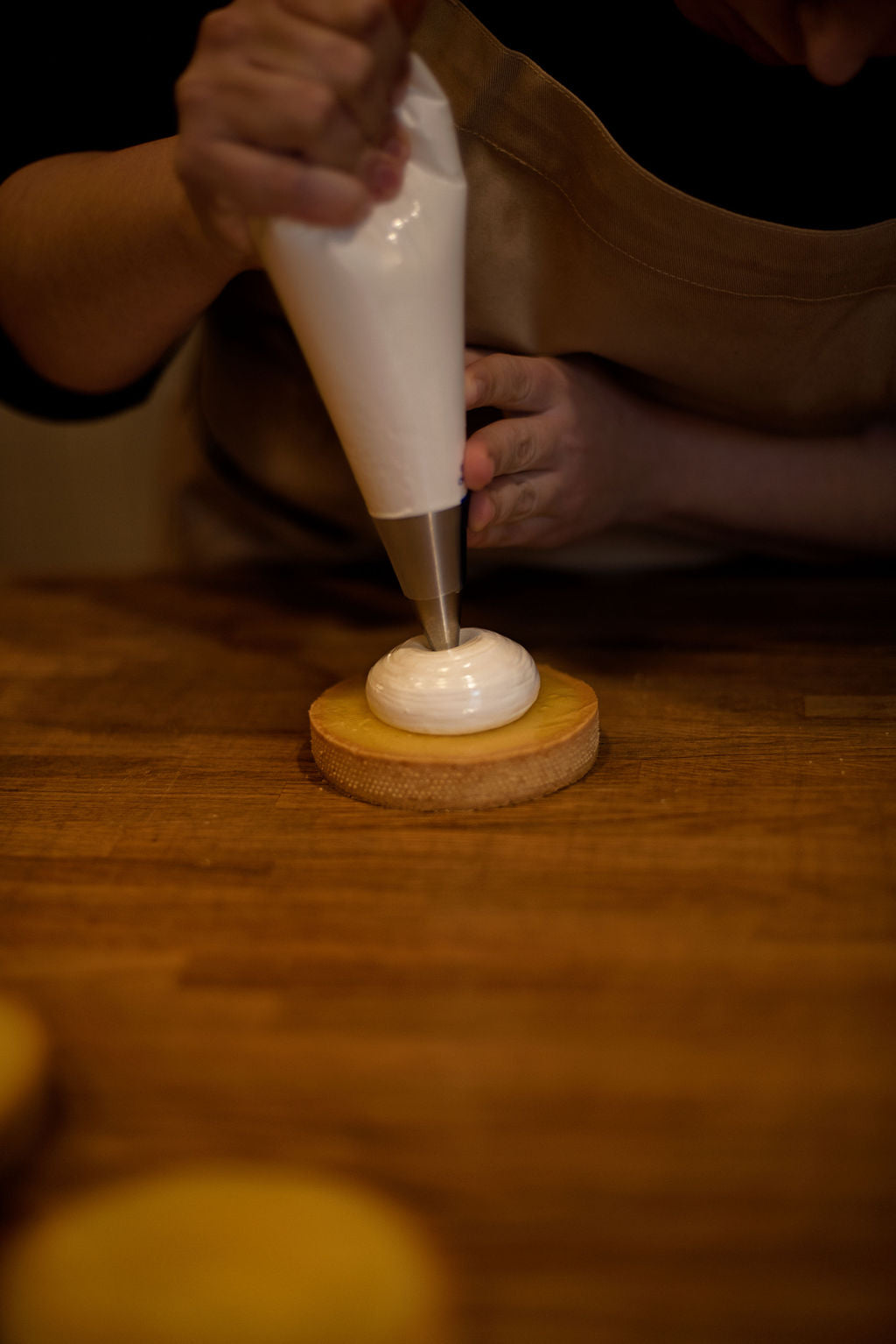 Piping a smooth spiral of Italian meringue from a pastry bag with a round tip onto a lemon curd-filled tart shell during a pastry class at Maison Fleuret Paris