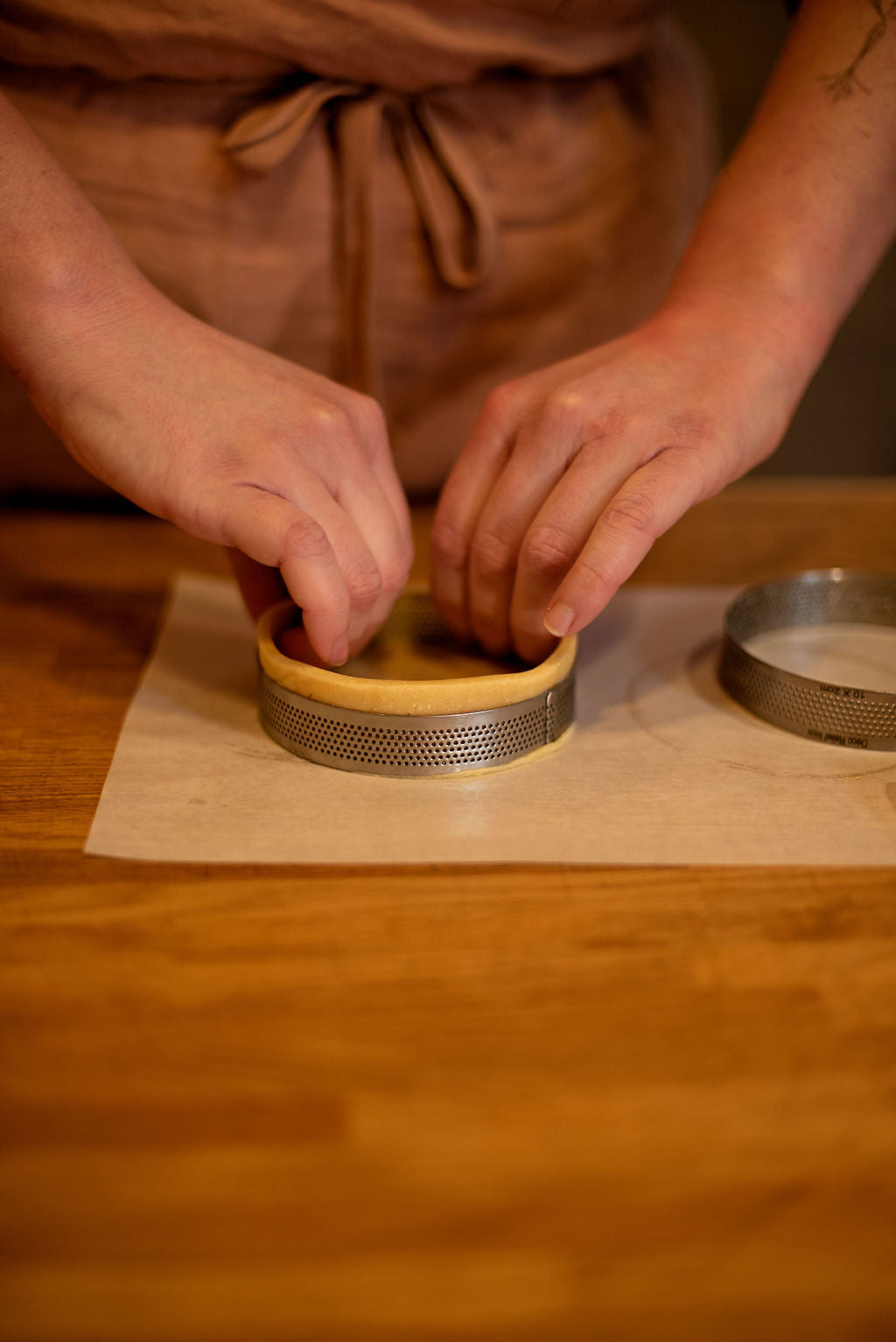 Close-up of hands pressing shortcrust pastry dough into a perforated tart ring on parchment paper to form a perfect tart shell during a lemon meringue class at Maison Fleuret Paris