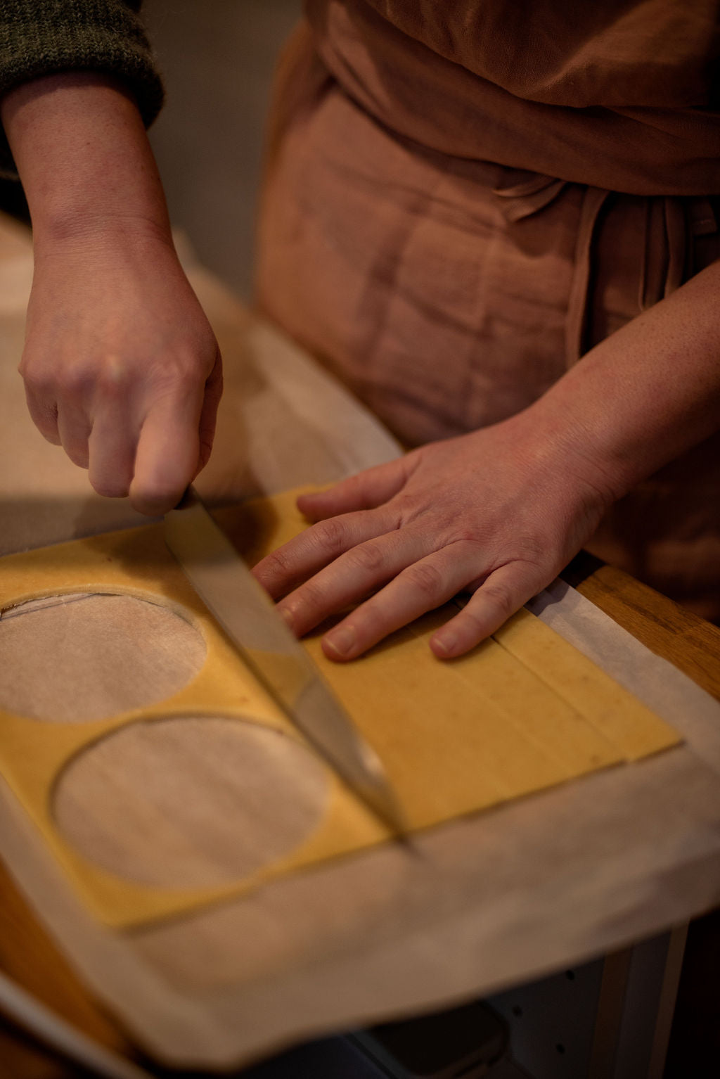 Participant in apron rolling out shortcrust pastry dough with a rolling pin between guide rails, with cut-out tart circles on parchment paper during a lemon meringue class at Maison Fleuret Paris