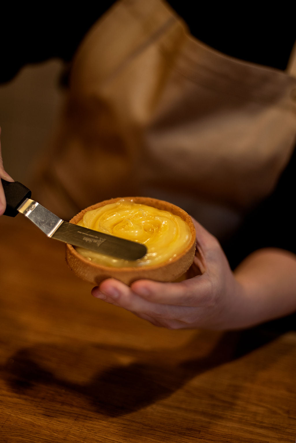 Hand spreading smooth lemon curd into a baked shortcrust tart shell with an offset spatula during a French lemon meringue tart class at Maison Fleuret Paris
