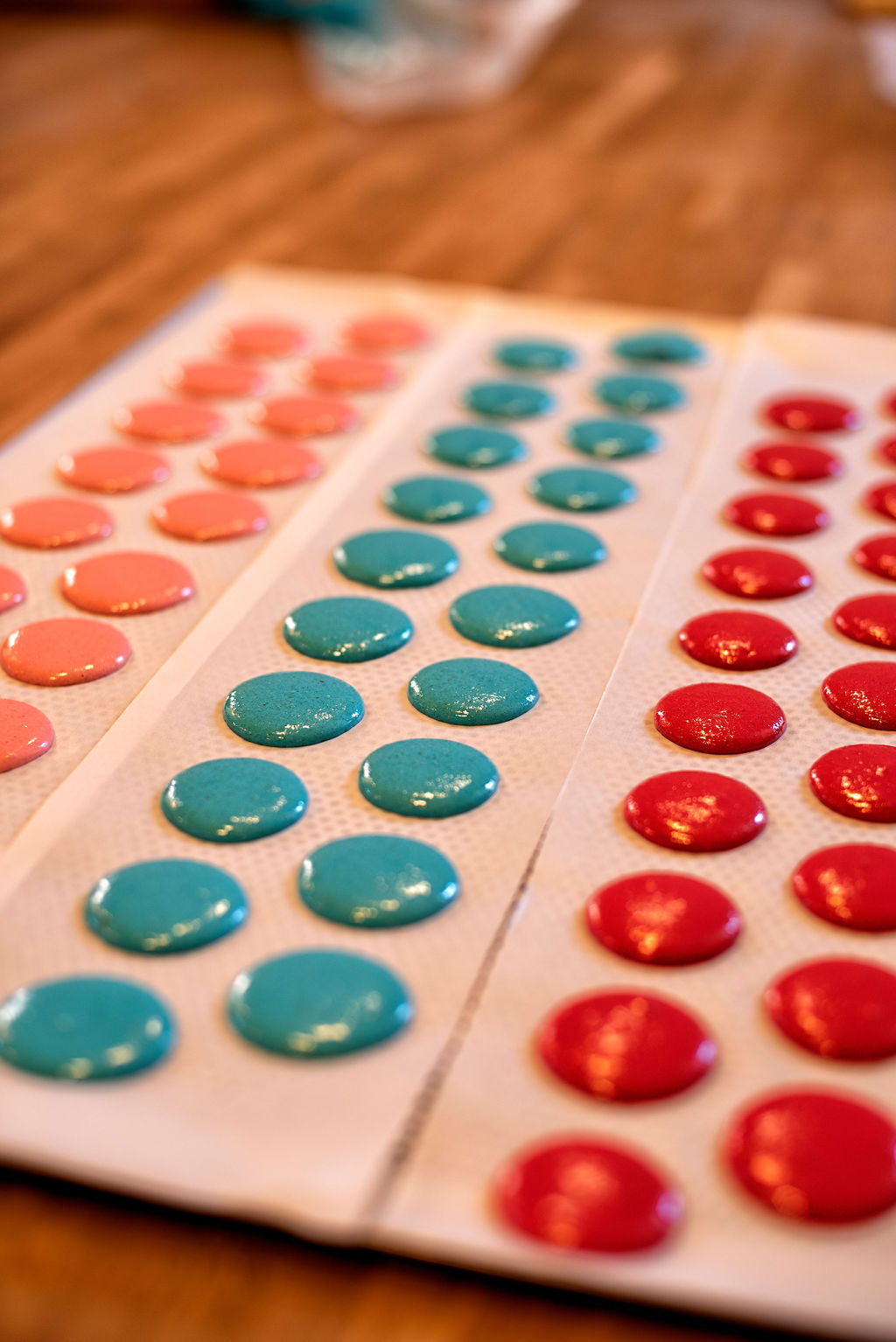 Rows of blue, red, and coral macaron shells freshly piped on baking trays during a Paris pastry workshop