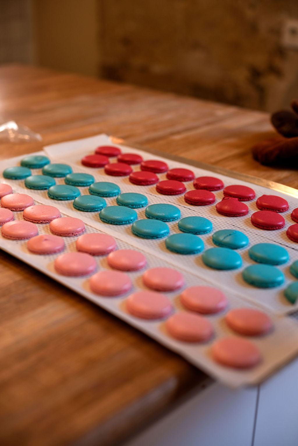 Close-up of colorful macaron shells — blue, coral, and orange — on a wooden table at Maison Fleuret Paris