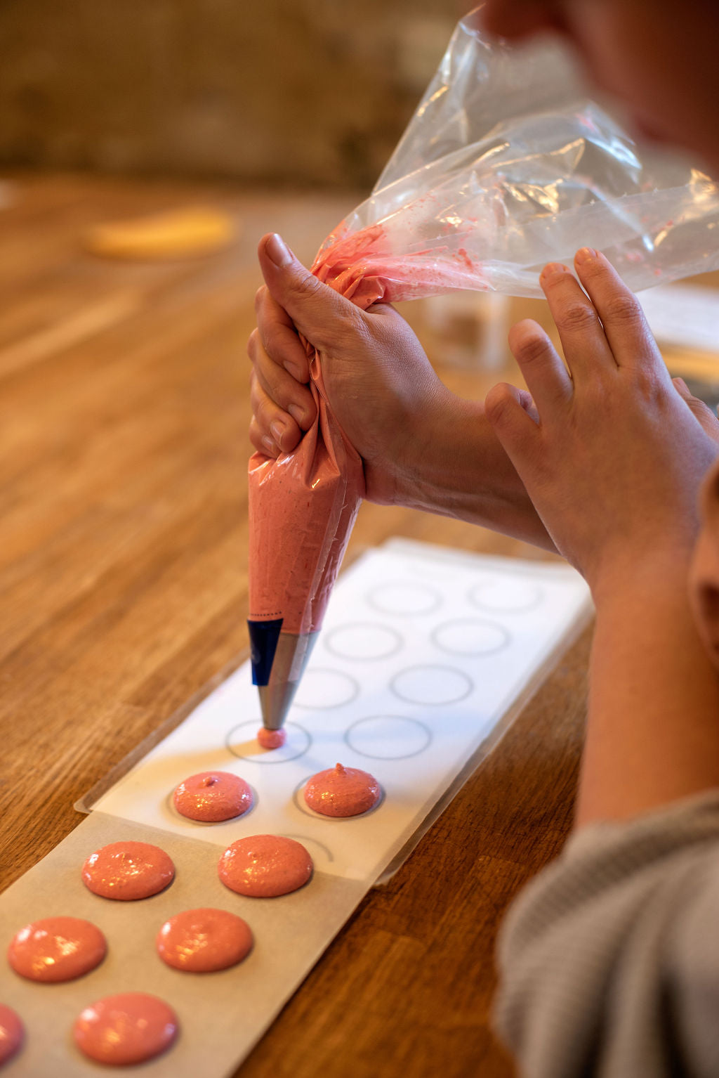 Hands piping perfectly round macaron shells onto parchment guided by a Maison Fleuret pastry chef