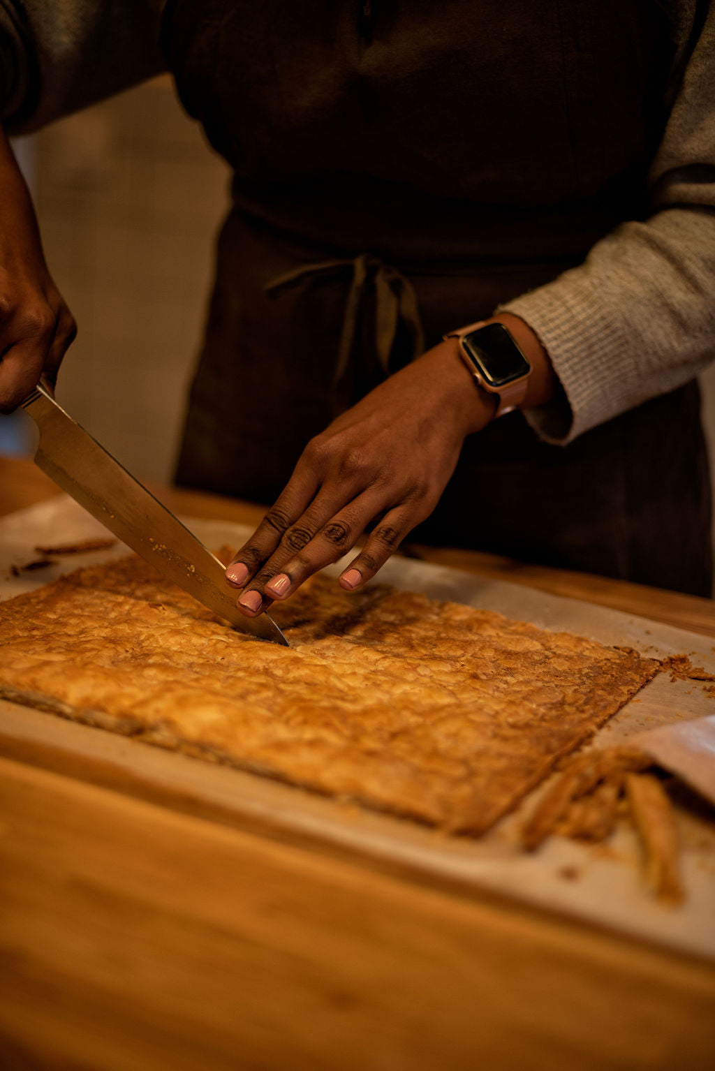 Participant in apron cutting a golden caramelized puff pastry sheet into precise rectangles with a serrated knife during a Napoleon millefeuille class at Maison Fleuret Paris