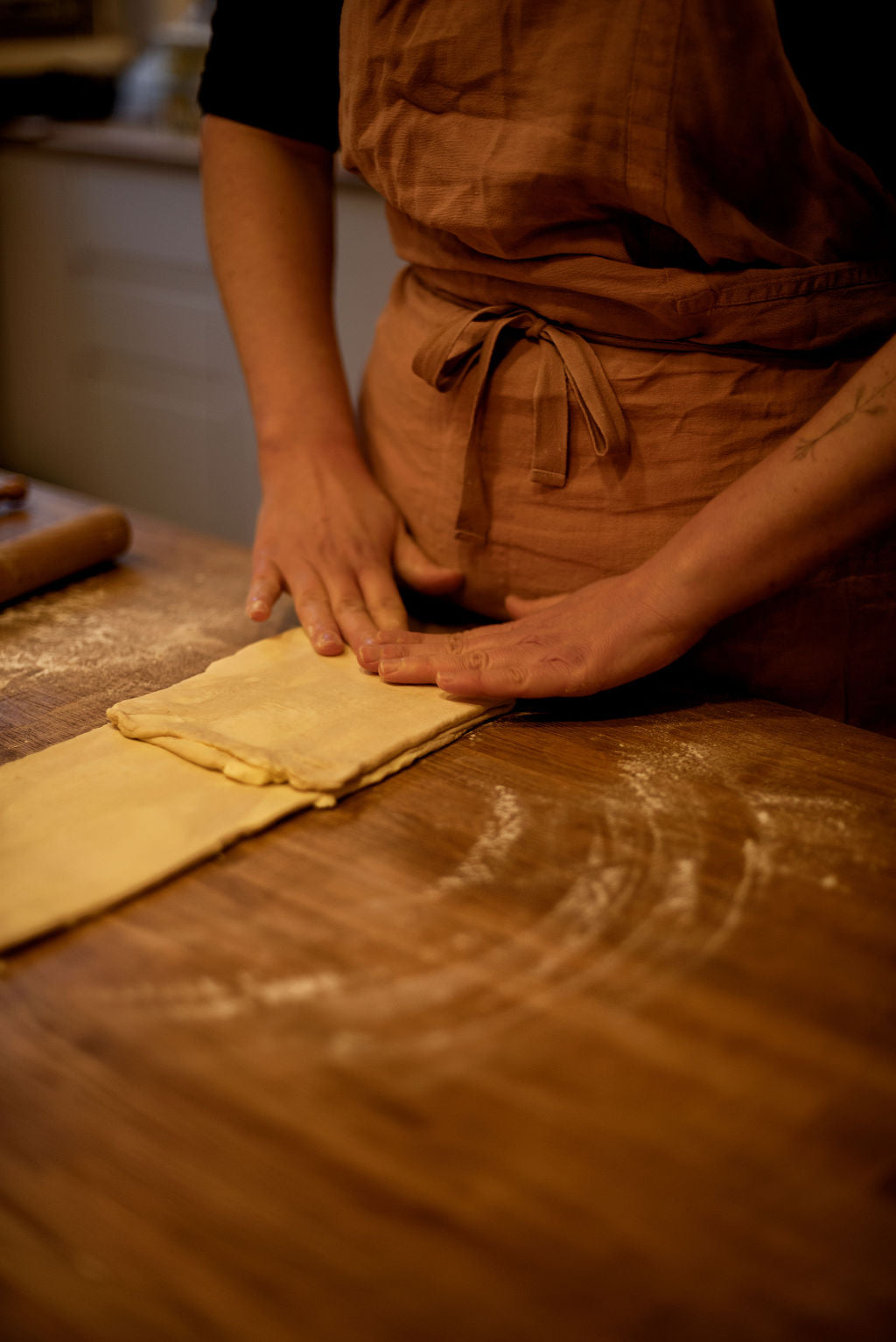 Participant in apron folding puff pastry dough to create buttery layers — the lamination technique — on a flour-dusted wooden table during a Napoleon millefeuille class at Maison Fleuret Paris