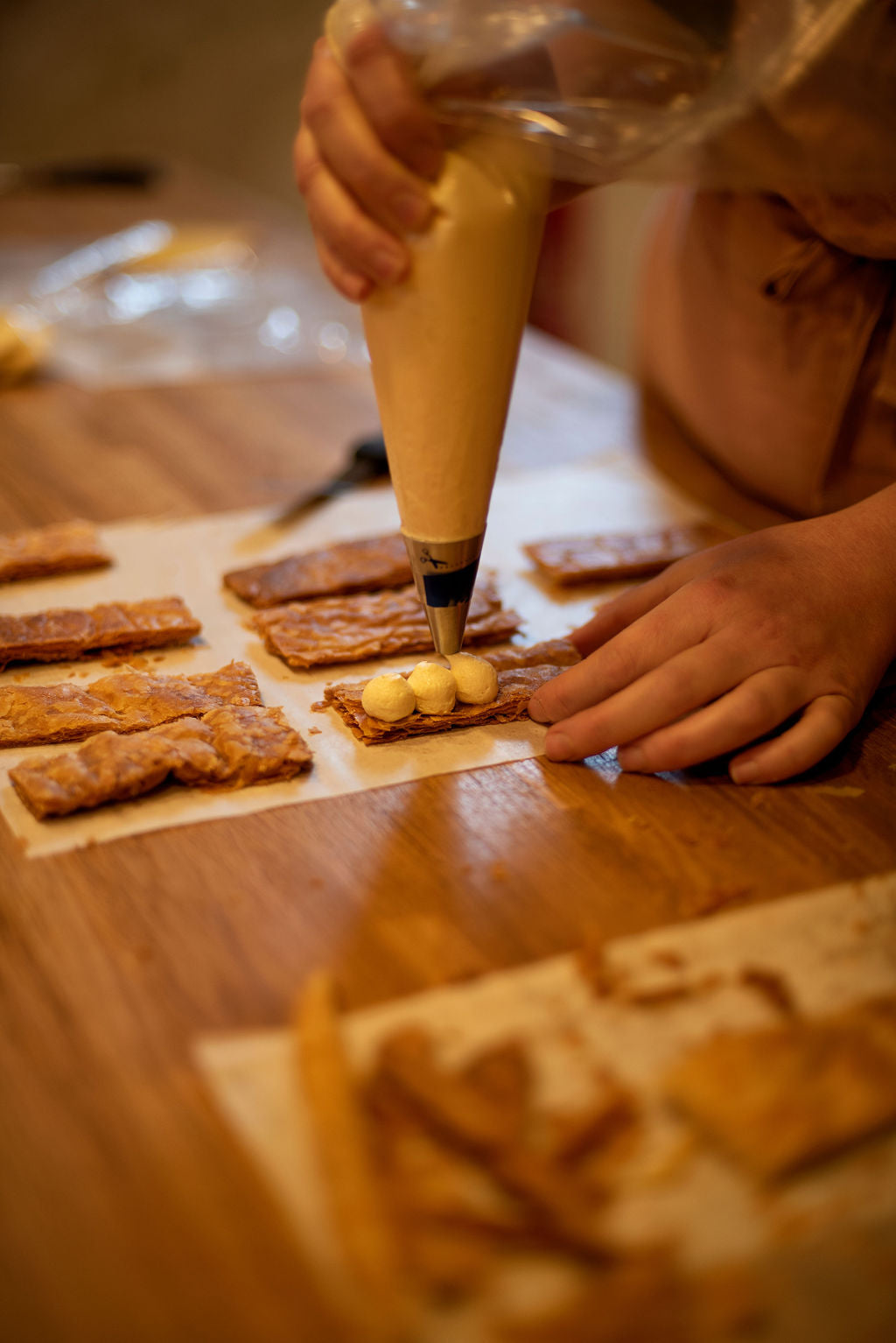 Participant piping pastry cream dots onto cut caramelized puff pastry rectangles to begin assembling individual millefeuilles during a Napoleon class at Maison Fleuret Paris