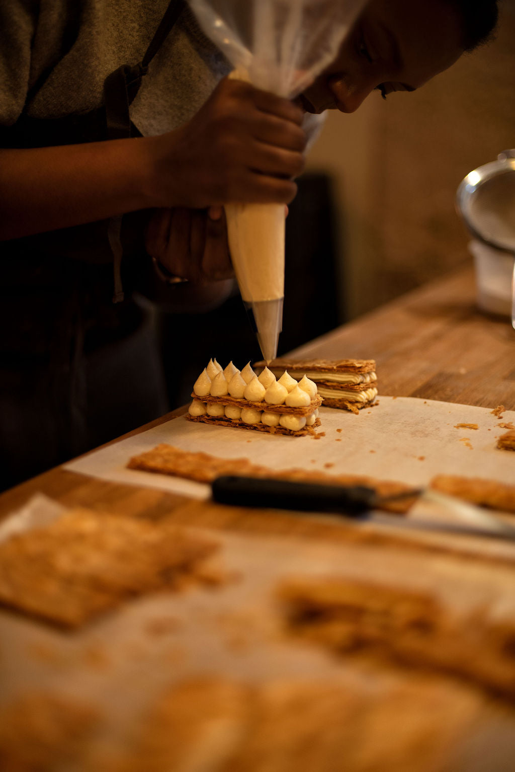 Participant piping rows of pastry cream drops onto layered puff pastry to assemble a millefeuille Napoleon during a hands-on pastry class at Maison Fleuret Paris