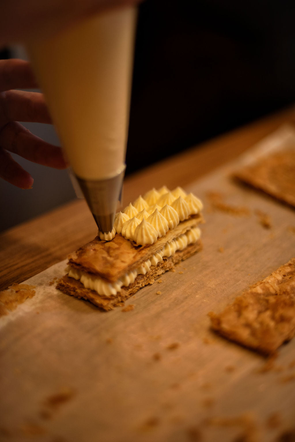 Close-up of piping precise star-tipped pastry cream peaks onto layered caramelized puff pastry to assemble an individual millefeuille during a Napoleon class at Maison Fleuret Paris