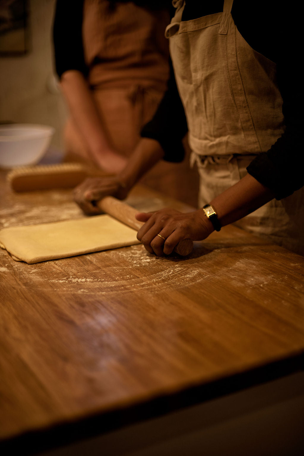 Two participants in aprons rolling out puff pastry dough with a wooden rolling pin on a flour-dusted table during a hands-on Napoleon millefeuille class at Maison Fleuret Paris