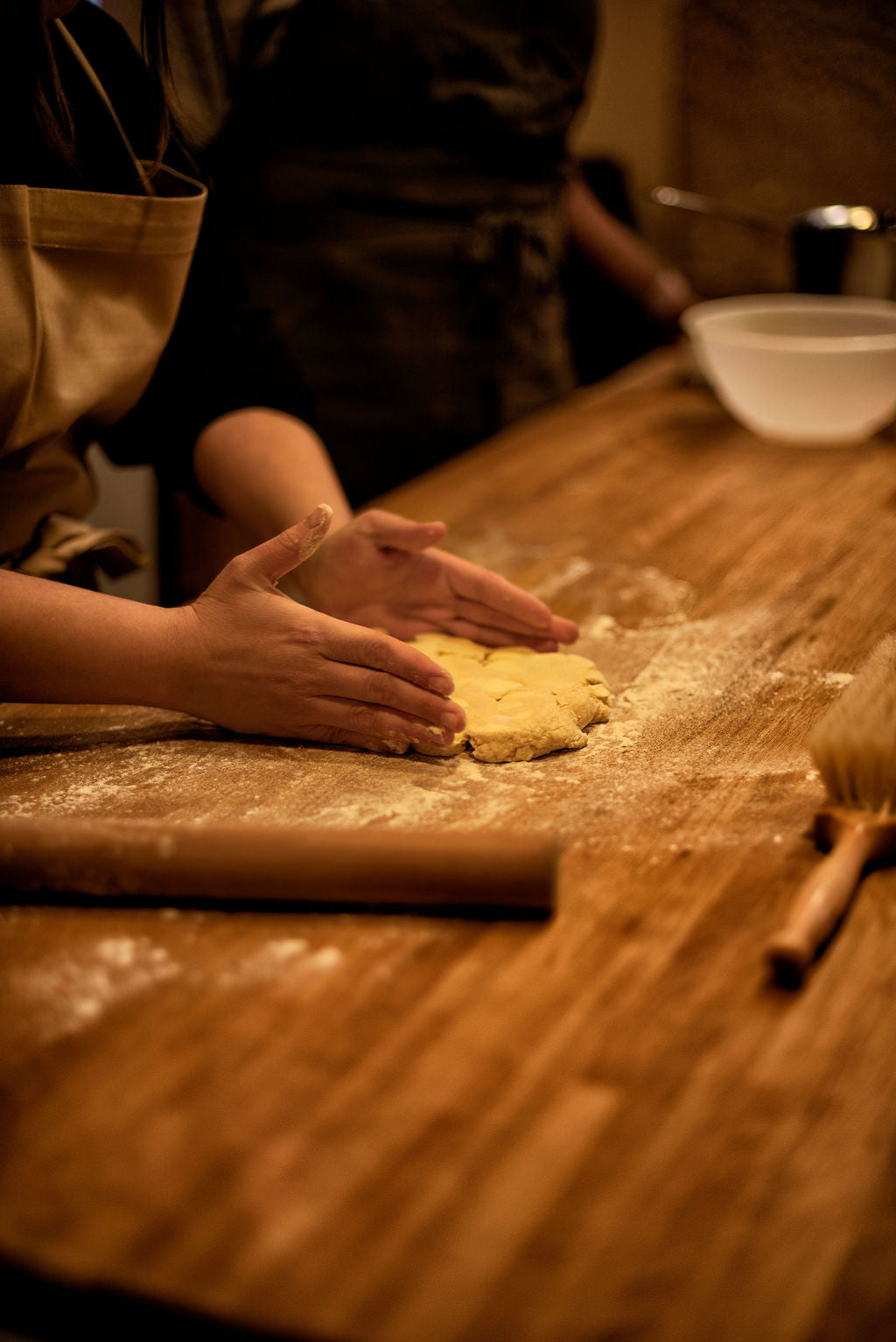 Participant shaping a butter and dough block by hand on a flour-dusted wooden table with a rolling pin and flour brush nearby during a Napoleon millefeuille class at Maison Fleuret Paris