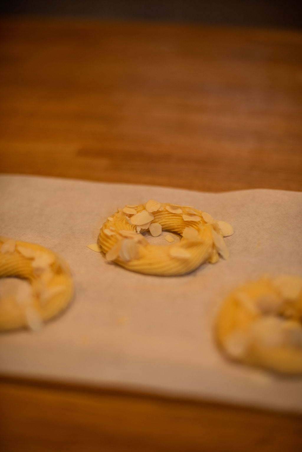 Close-up of a piped choux pastry ring topped with slivered almonds on parchment paper ready for baking, the signature Paris-Brest wheel shape, during a class at Maison Fleuret Paris