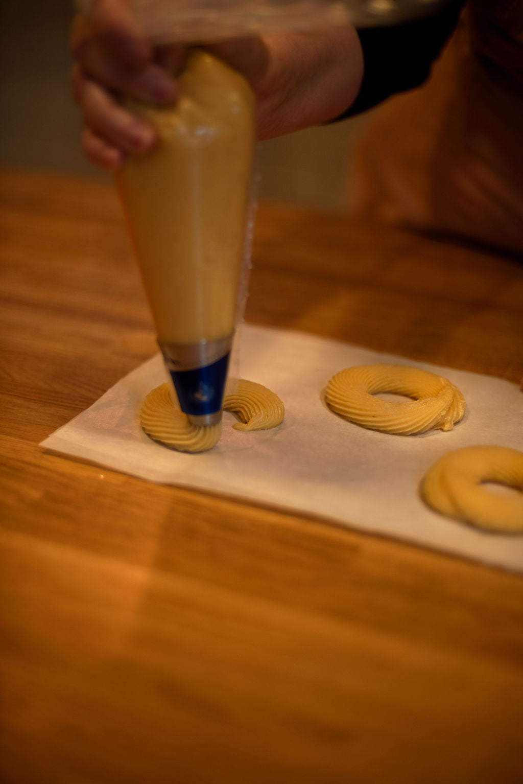 Piping choux pastry dough into ring shapes on parchment paper with a pastry bag and ridged tip to form the signature Paris-Brest wheel shape during a class at Maison Fleuret Paris