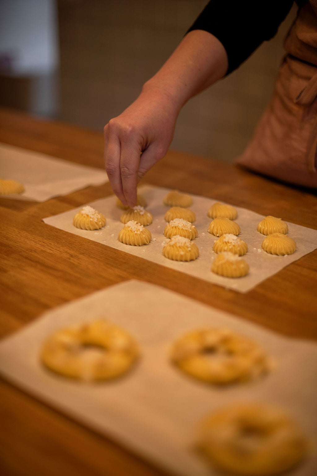 Hand sprinkling pearl sugar over piped choux buns and Paris-Brest rings on parchment paper before baking during a hands-on pastry class at Maison Fleuret Paris