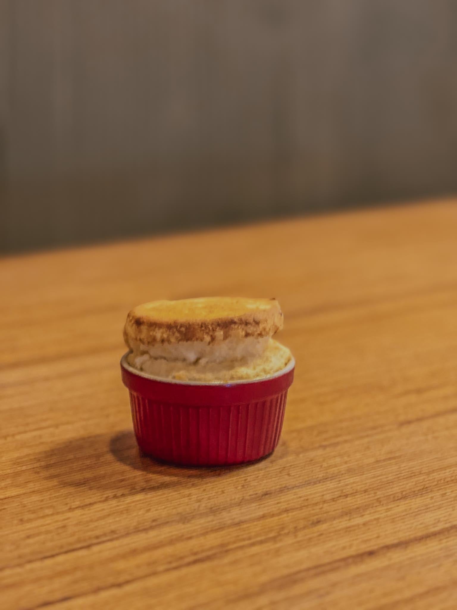 Perfectly risen French souffle dramatically puffed above a red ceramic ramekin on a wooden table — the signature moment of a souffle baking class at Maison Fleuret Paris near Notre-Dame