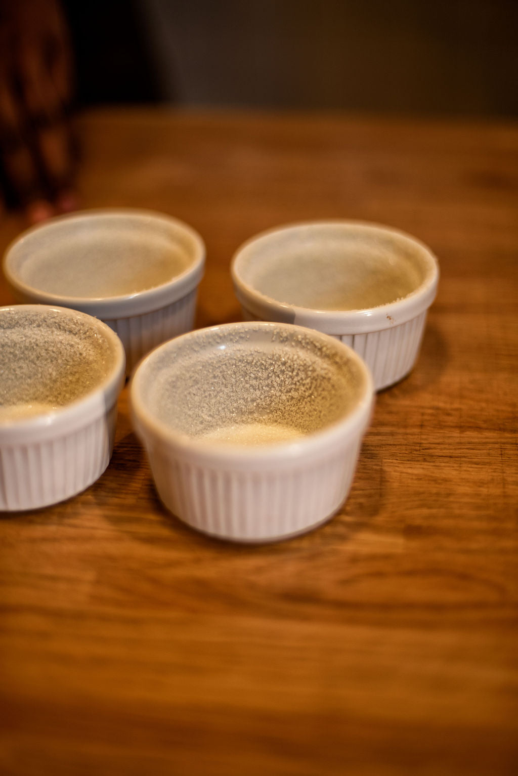 White ceramic ramekins buttered and coated with sugar — the essential preparation step for a perfect rise — on a wooden table during a French souffle class at Maison Fleuret Paris near Notre-Dame